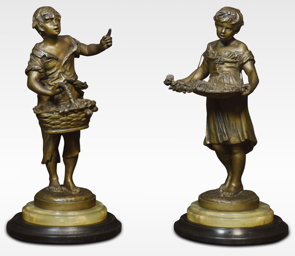 A pair of bronzed French spelter figures depicting a young boy with a basket and a young girl with a tray on alabaster and wooden bases.