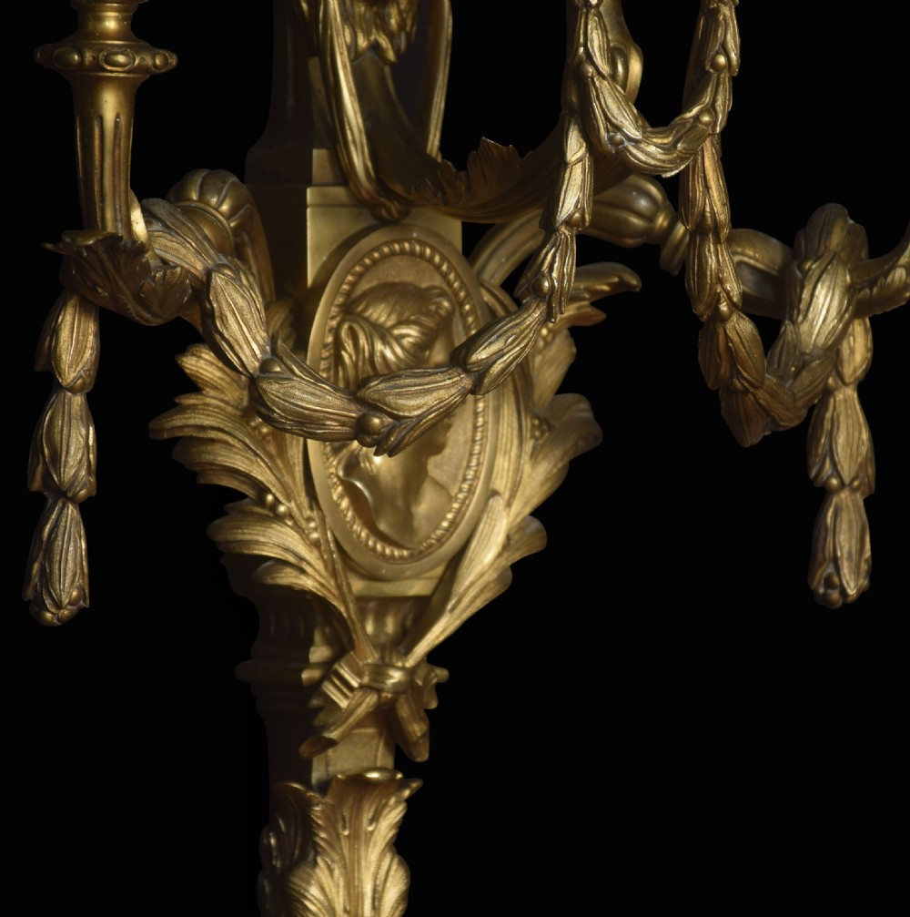 A pair of gilded bronze Louis XVI style three-arm wall lights decorated with classical profile medallions, laurel swags, and acanthus leaf details. View VIII