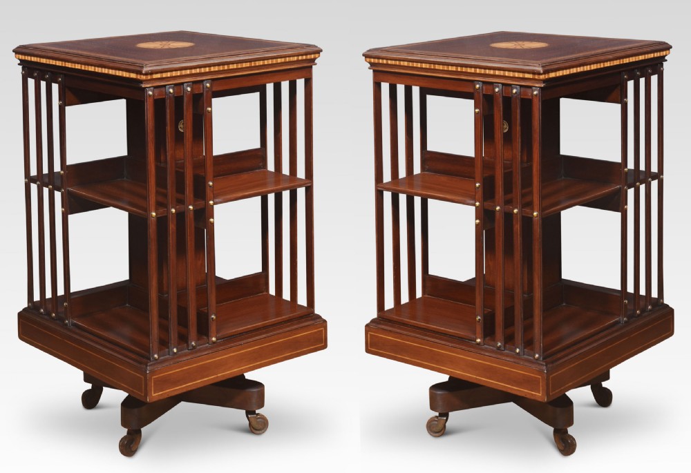 A pair of Edwardian inlaid mahogany revolving bookcases featuring square tops with satinwood crossbanding, vertical slat sides, and rotating bases on castors. View V