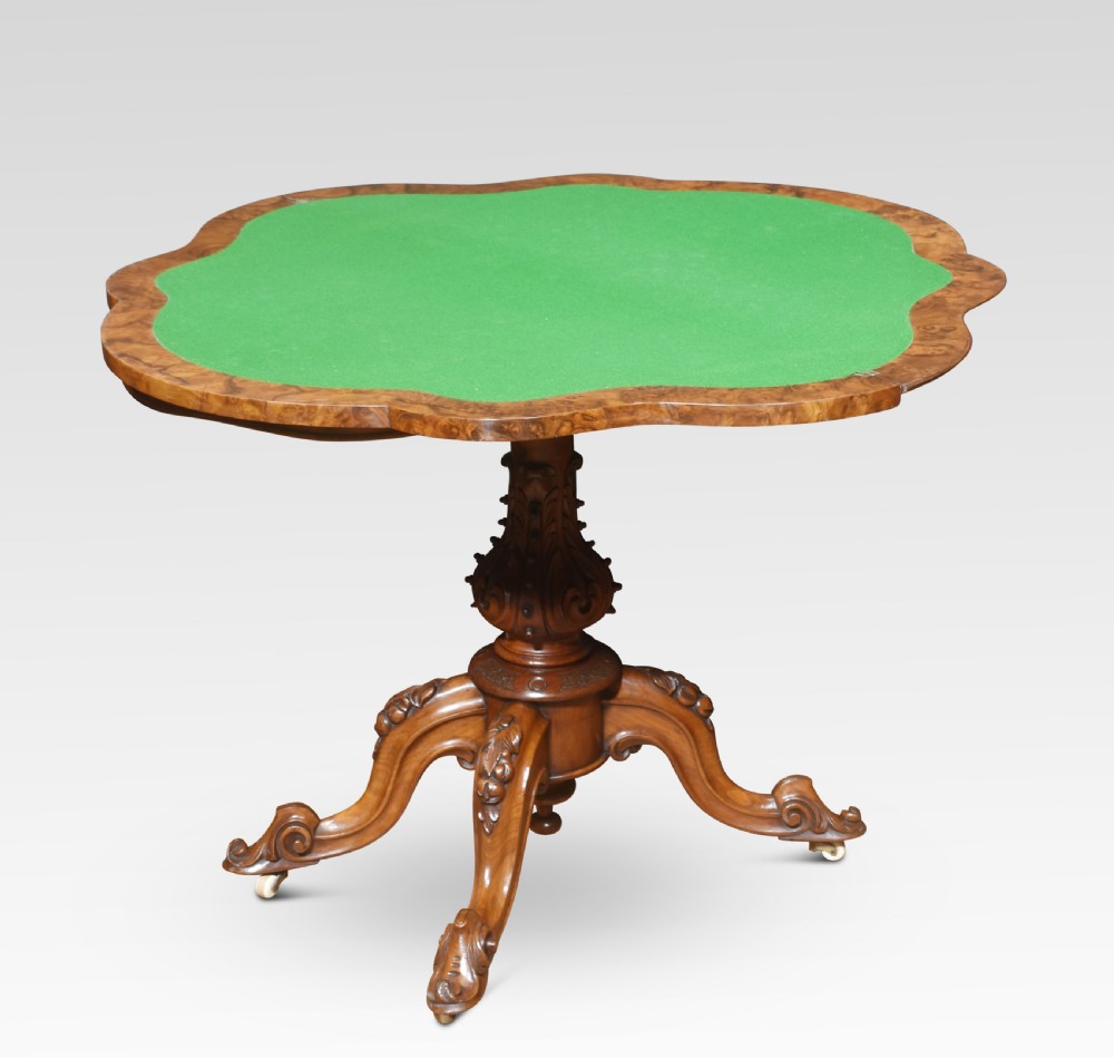 An antique Victorian burr walnut card table featuring a shaped serpentine top lined with green baize, resting on a carved pedestal stem and tripod cabriole legs.