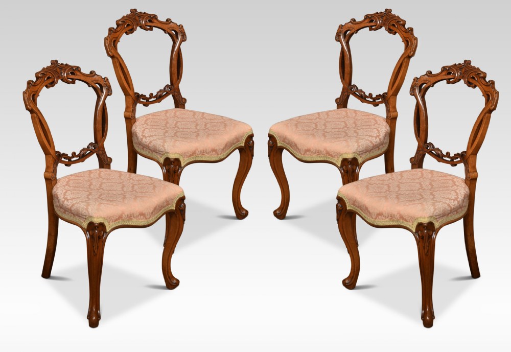 A set of four Victorian walnut salon chairs with rounded balloon backs, carved crests, patterned light pink upholstered seats, and cabriole legs.