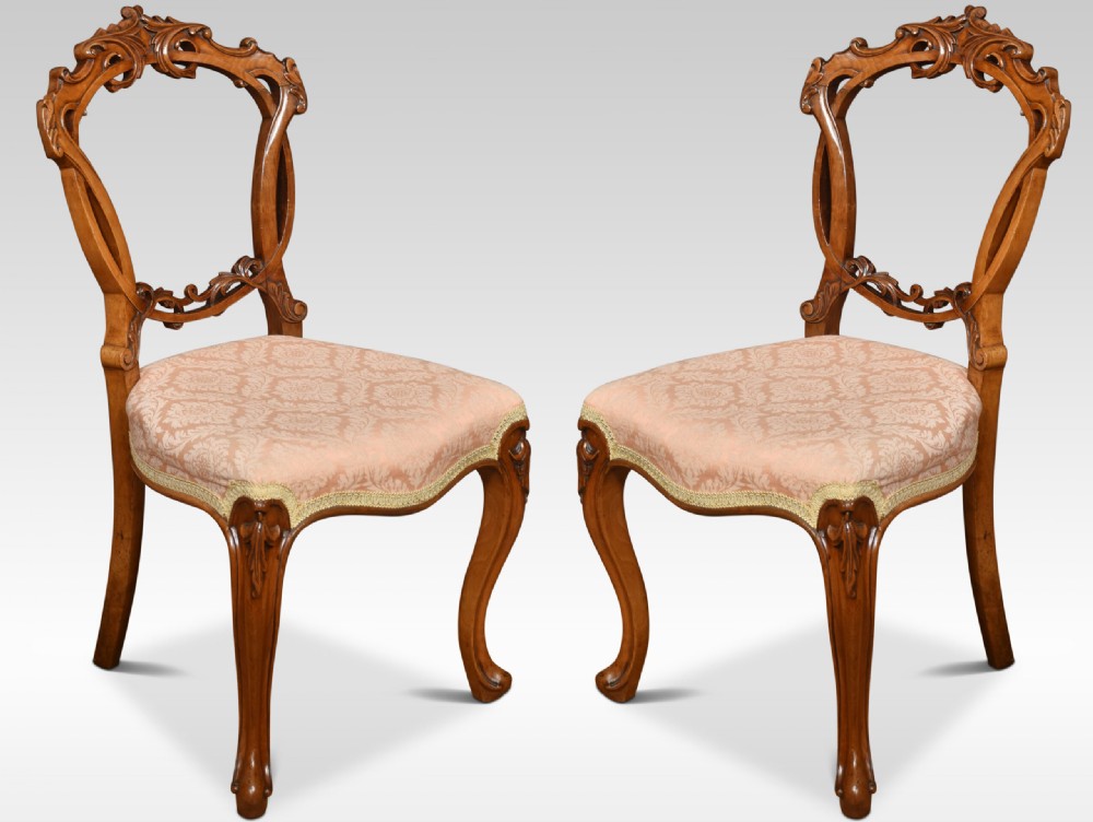 A set of four Victorian walnut salon chairs with rounded balloon backs, carved crests, patterned light pink upholstered seats, and cabriole legs. View II