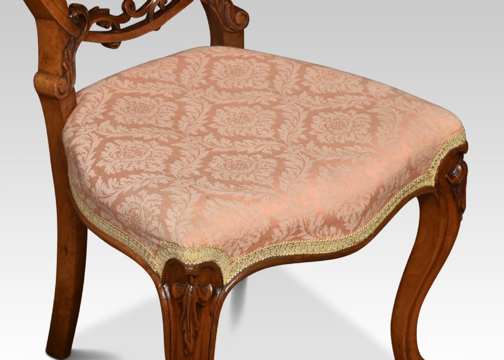 A set of four Victorian walnut salon chairs with rounded balloon backs, carved crests, patterned light pink upholstered seats, and cabriole legs. View V