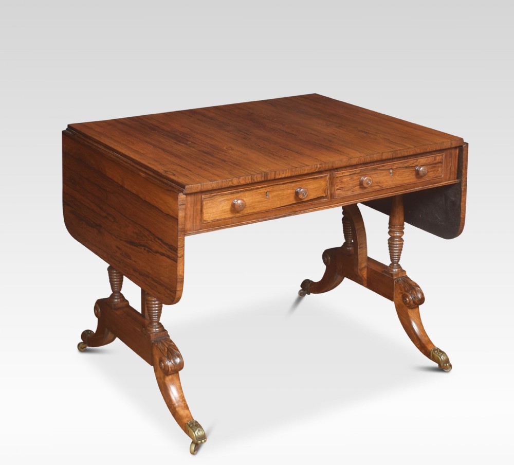 A Regency rosewood sofa table with two drop flaps, two frieze drawers with turned timber knobs, double pillar supports, and splayed legs ending in brass castors.