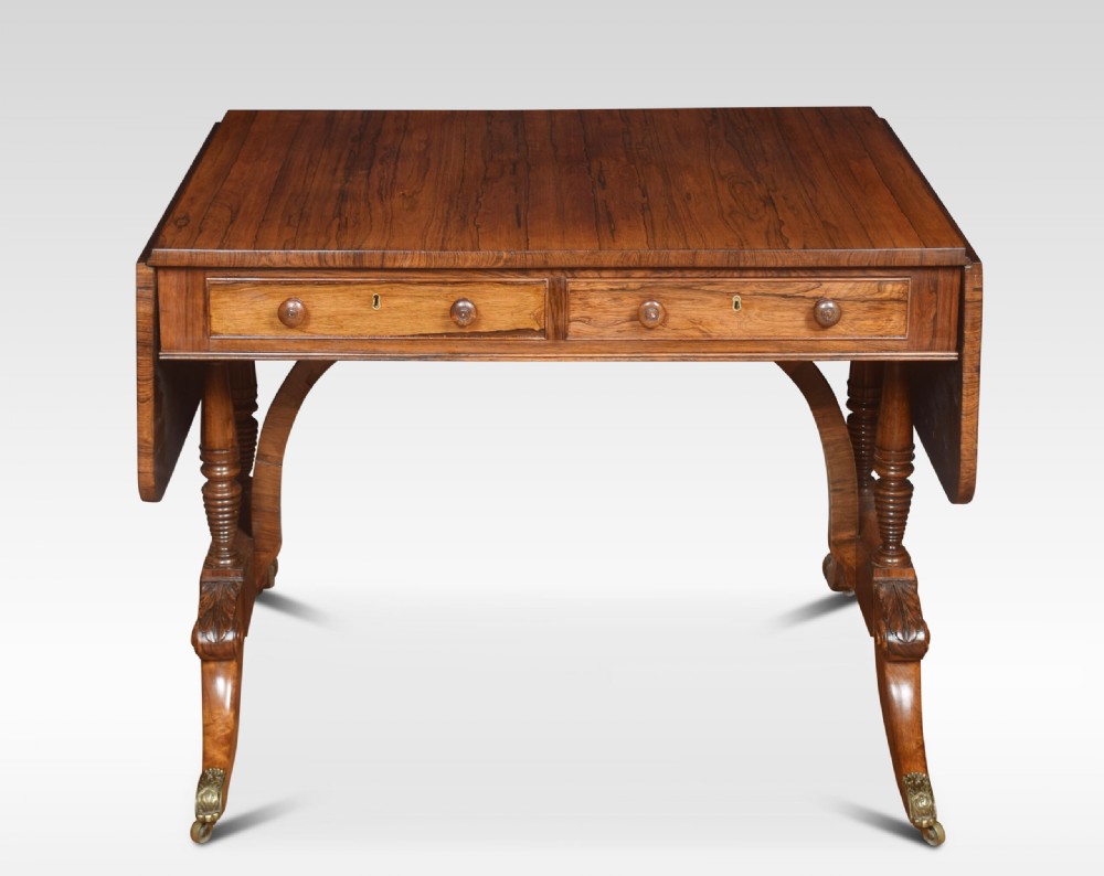 A Regency rosewood sofa table with two drop flaps, two frieze drawers with turned timber knobs, double pillar supports, and splayed legs ending in brass castors. View II
