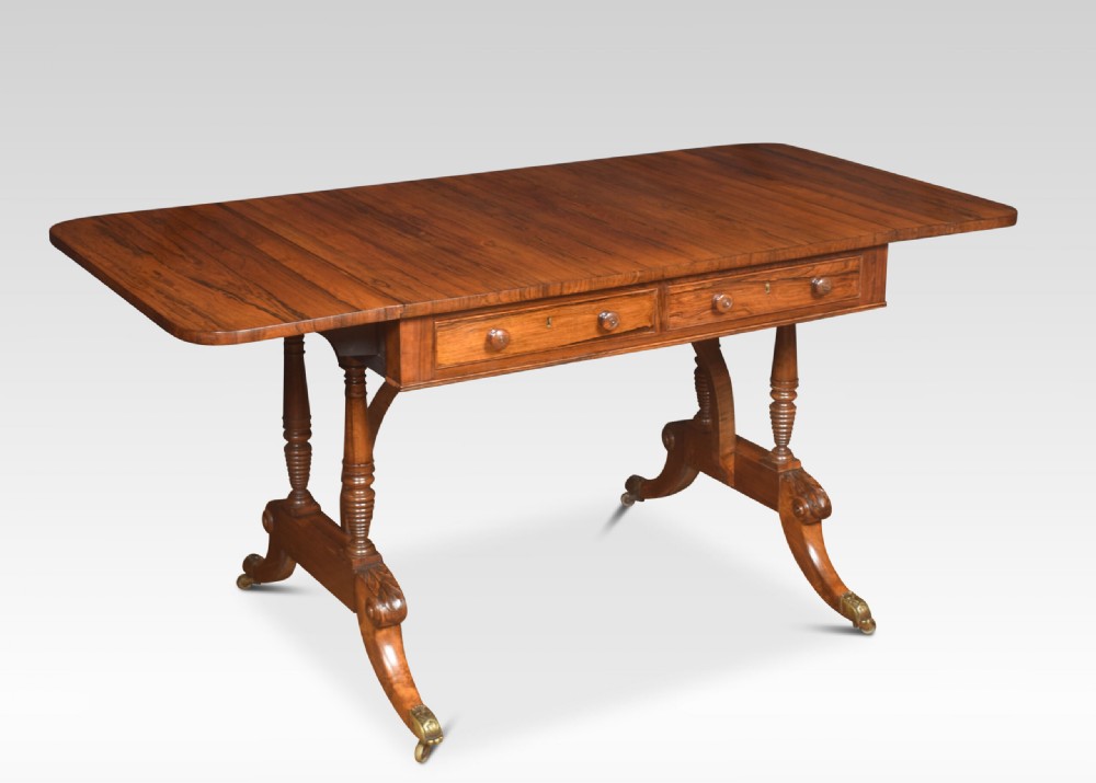 A Regency rosewood sofa table with two drop flaps, two frieze drawers with turned timber knobs, double pillar supports, and splayed legs ending in brass castors. View VI