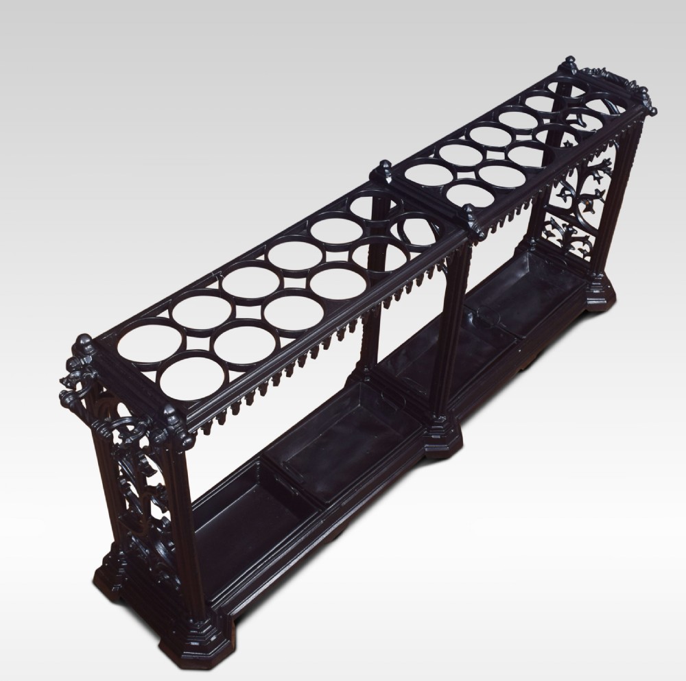 A long black cast iron umbrella stand featuring twenty-four circular rings supported by decorative pierced side panels and integrated base drip trays.