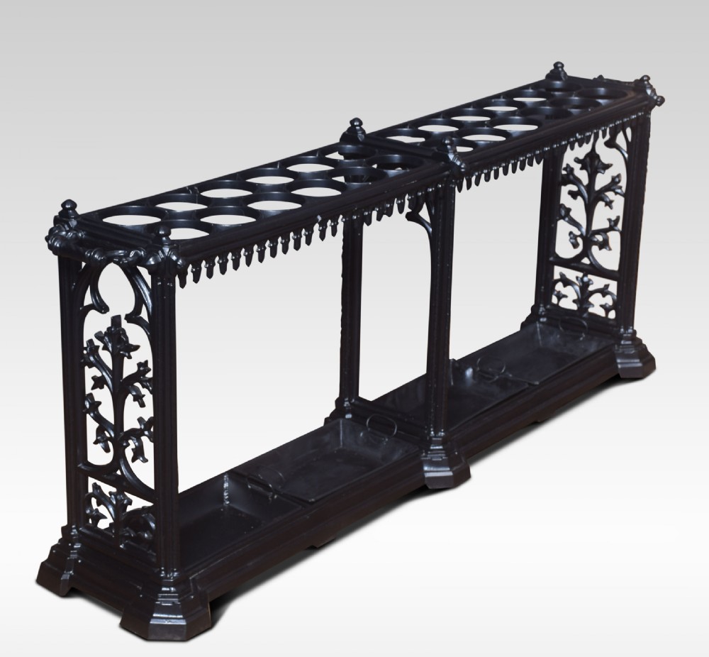 A long black cast iron umbrella stand featuring twenty-four circular rings supported by decorative pierced side panels and integrated base drip trays. View III