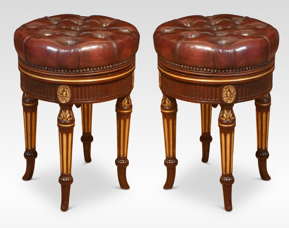 A pair of 19th-century circular adjustable stools featuring deep button-tufted chestnut brown leather upholstery, parcel-gilded details, and fluted turned legs.