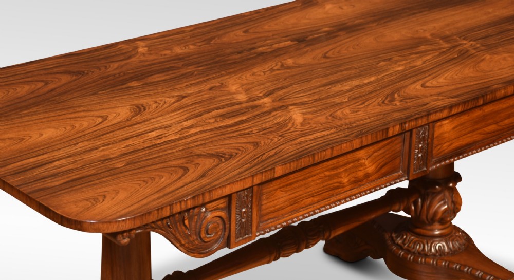 A Regency rosewood library table featuring a rectangular top, twin carved pedestal supports, a turned cross stretcher, and lion paw feet. View II