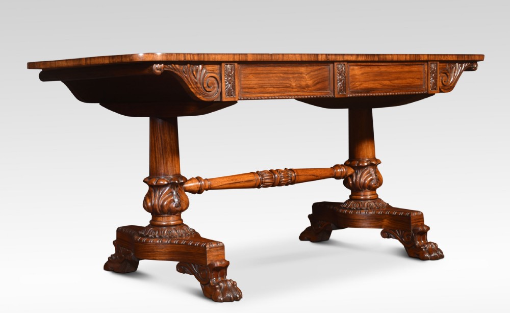 A Regency rosewood library table featuring a rectangular top, twin carved pedestal supports, a turned cross stretcher, and lion paw feet. View VI