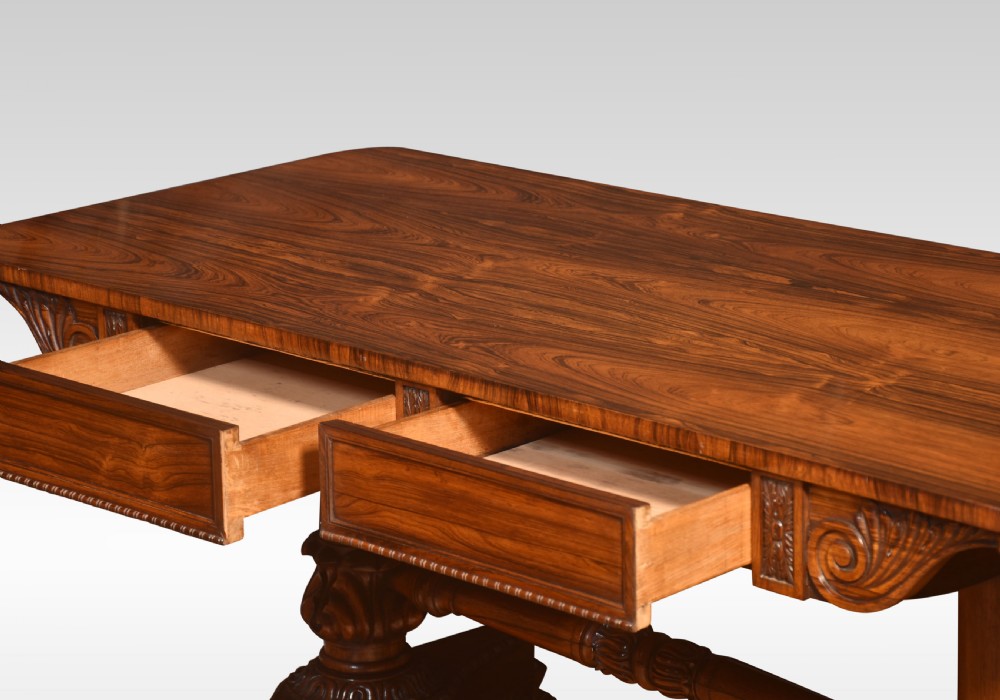 A Regency rosewood library table featuring a rectangular top, twin carved pedestal supports, a turned cross stretcher, and lion paw feet. View X