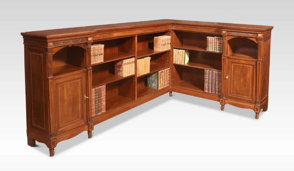 An L-shaped antique mahogany open corner bookcase featuring satinwood inlaid stringing, central open shelves, and flanking side cupboards.
