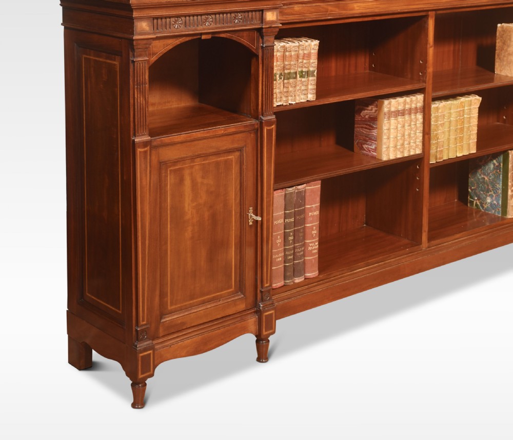 An L-shaped antique mahogany open corner bookcase featuring satinwood inlaid stringing, central open shelves, and flanking side cupboards. View V