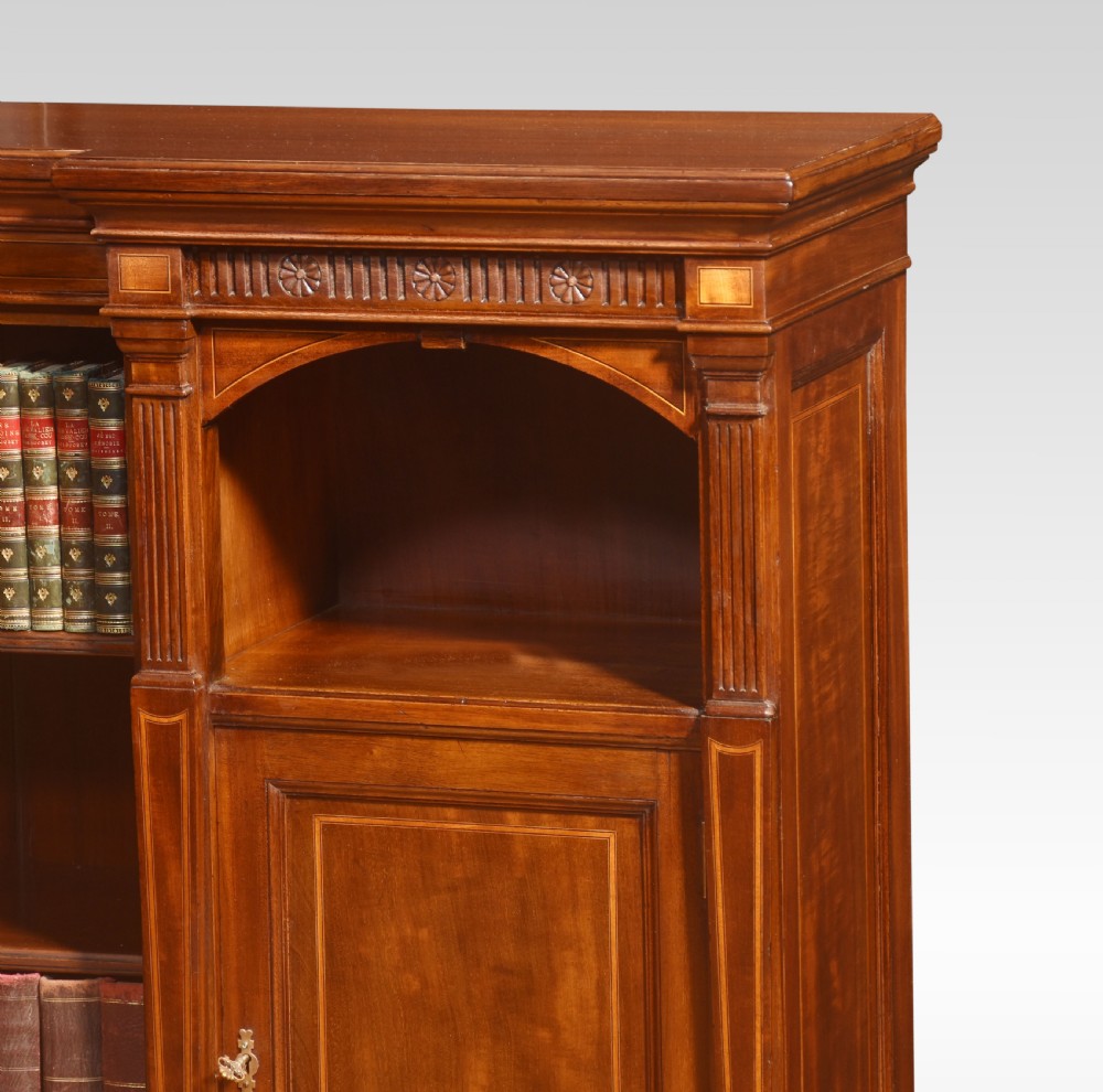 An L-shaped antique mahogany open corner bookcase featuring satinwood inlaid stringing, central open shelves, and flanking side cupboards. View VI