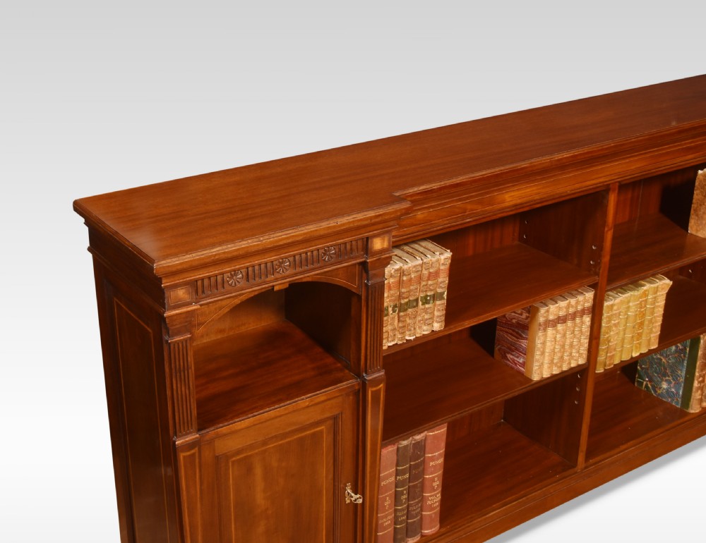 An L-shaped antique mahogany open corner bookcase featuring satinwood inlaid stringing, central open shelves, and flanking side cupboards. View VII