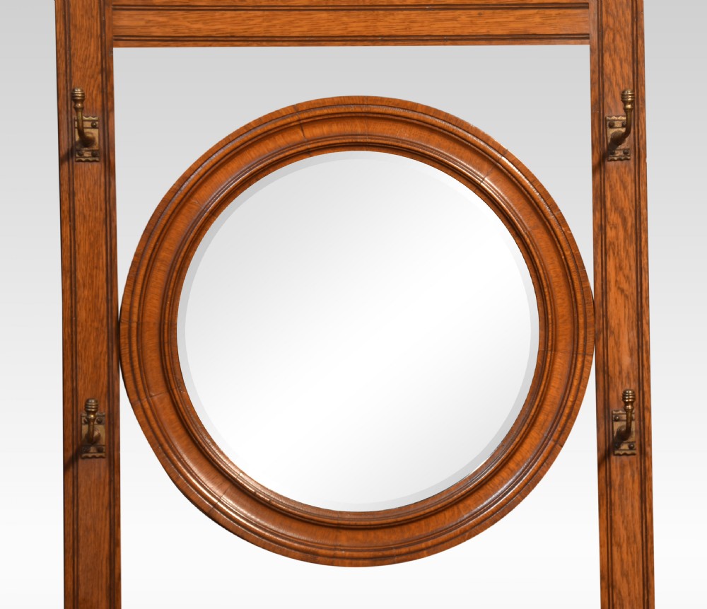 An antique carved oak hall stand featuring a central circular mirror, upper coat hooks, a small shelf above a single drawer, and side umbrella stands with lower trays. View II