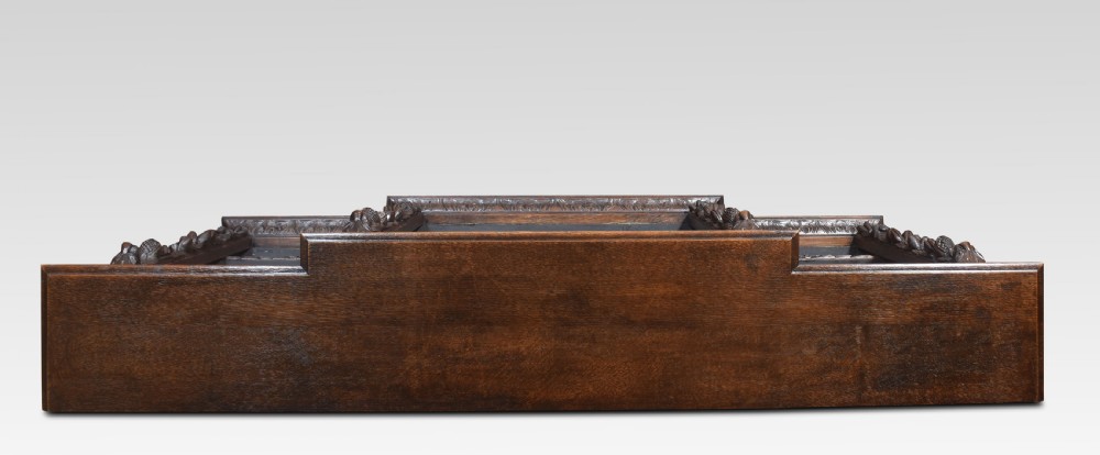 A low, dark carved oak open bookcase with a breakfront design, featuring three shelf sections separated by carved pilasters decorated with foliate and mask motifs. View XV