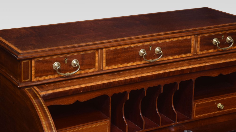 An antique mahogany cylinder desk featuring floral marquetry inlay, brass drop handles, square tapered legs, and an upper tier with drawers. View III