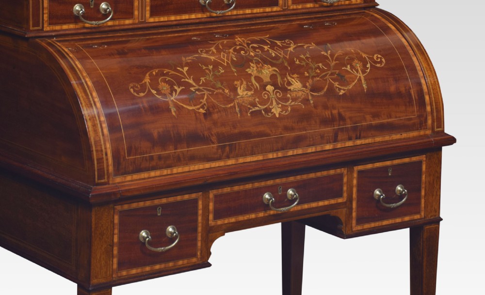 An antique mahogany cylinder desk featuring floral marquetry inlay, brass drop handles, square tapered legs, and an upper tier with drawers. View V