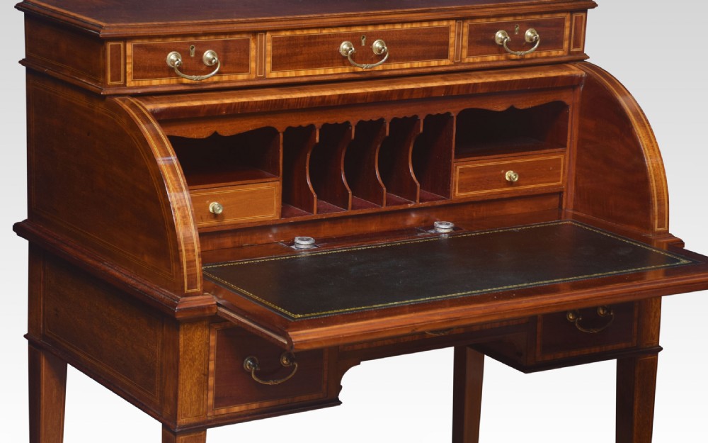 An antique mahogany cylinder desk featuring floral marquetry inlay, brass drop handles, square tapered legs, and an upper tier with drawers. View VII
