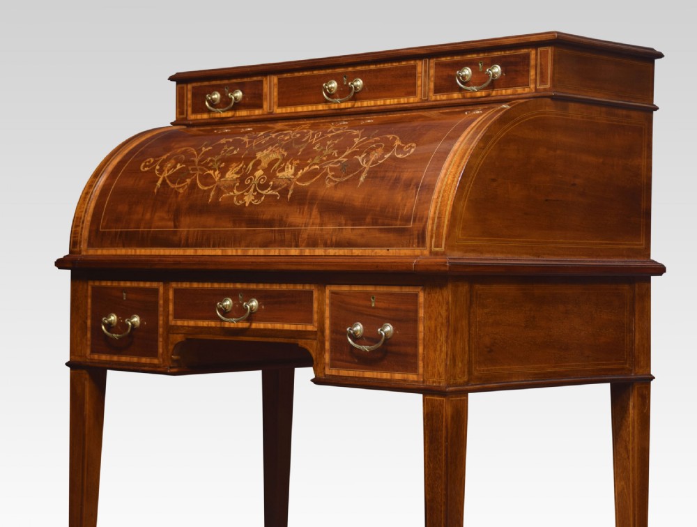 An antique mahogany cylinder desk featuring floral marquetry inlay, brass drop handles, square tapered legs, and an upper tier with drawers. View IX