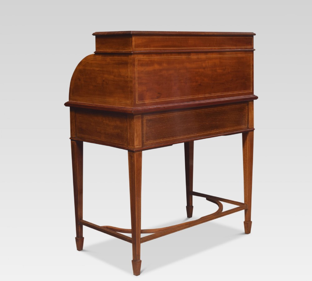 An antique mahogany cylinder desk featuring floral marquetry inlay, brass drop handles, square tapered legs, and an upper tier with drawers. View X