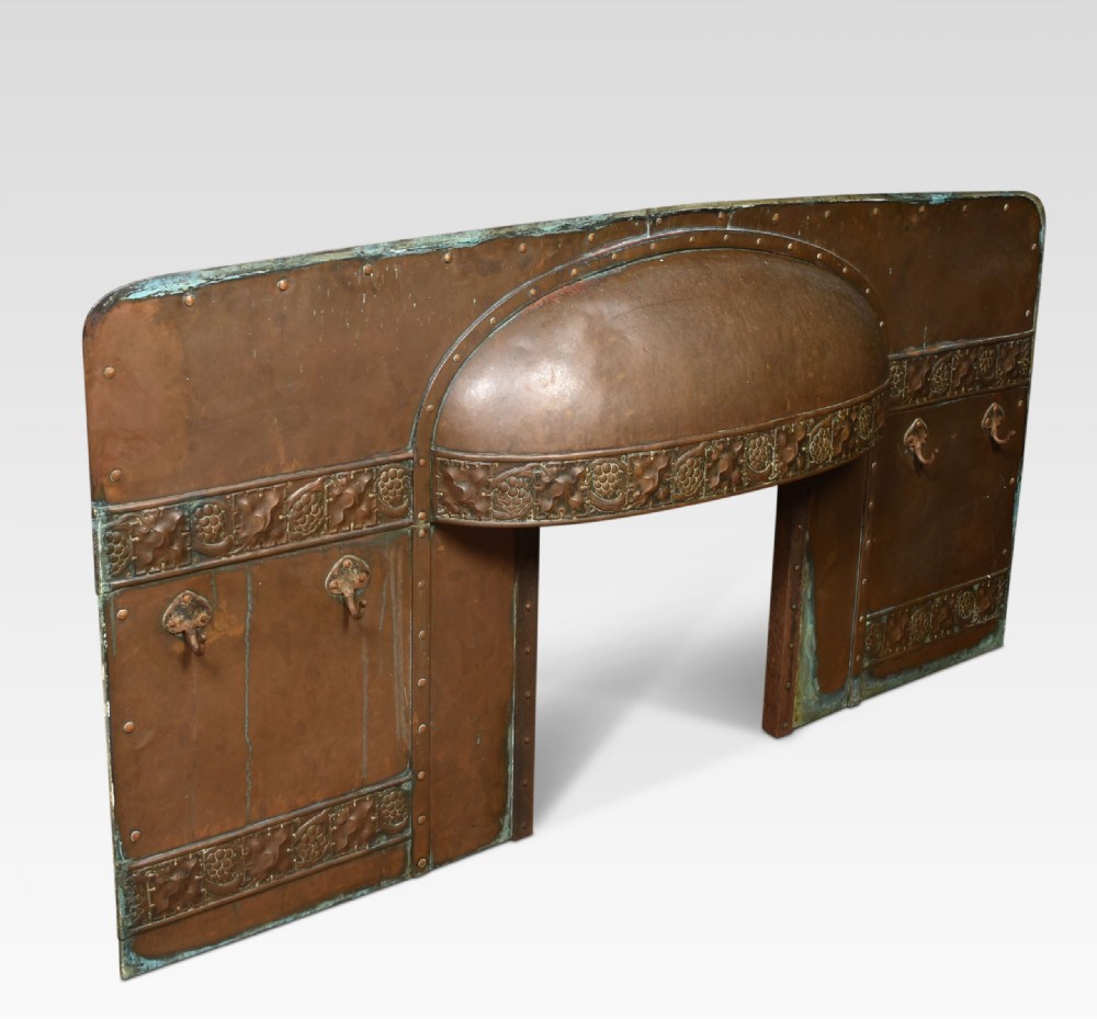 An Arts and Crafts period embossed copper fireplace insert featuring a central domed canopy, riveted construction, and foliage repousse panels.