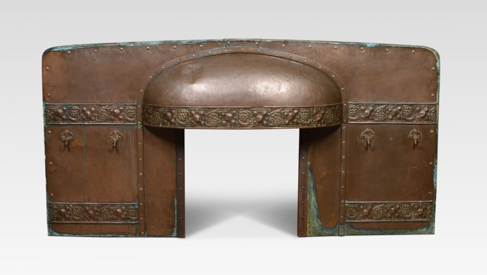 An Arts and Crafts period embossed copper fireplace insert featuring a central domed canopy, riveted construction, and foliage repousse panels. View II