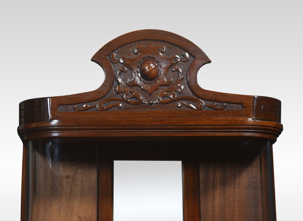 An antique mahogany bow-fronted display cabinet featuring curved glass sides, a mirrored back panel, and a carved cresting pediment at the top. View III