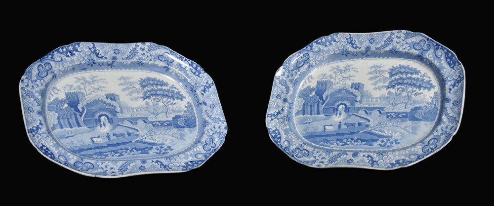 A pair of oblong blue and white transferware ceramic platters decorated with classical landscape scenes and floral borders.