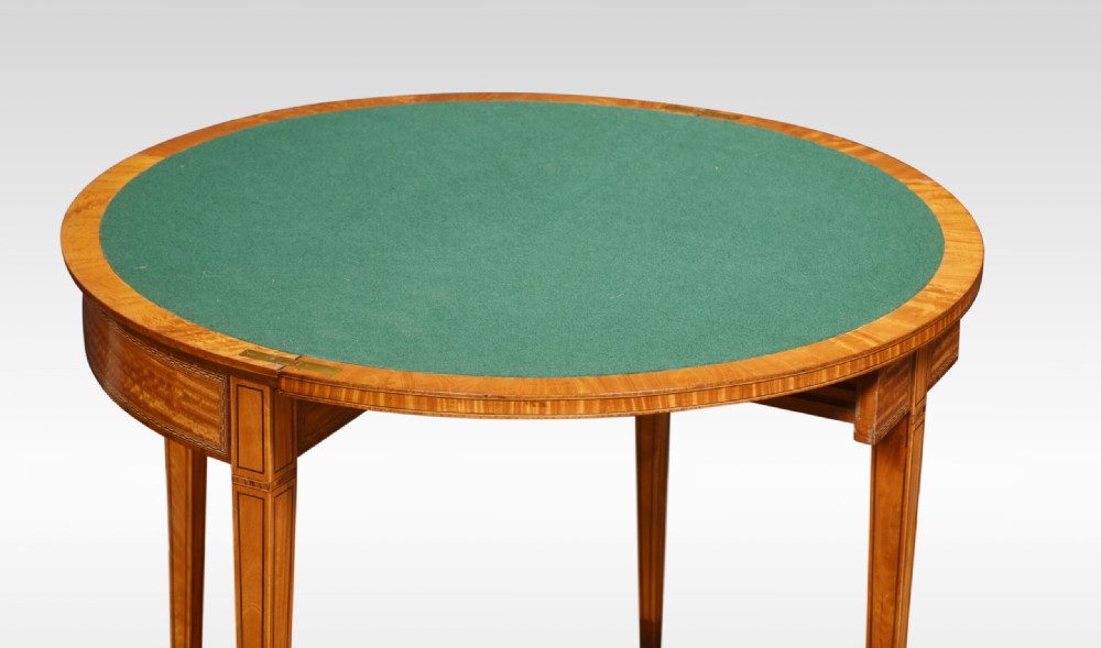 An antique semi-circular satinwood card table featuring inlaid crossbanding, tapered square legs, and small brass castors. View III