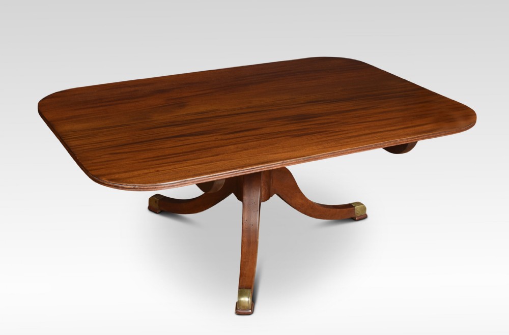 A low rectangular mahogany coffee table with rounded corners, resting on a central turned pedestal base with four splayed legs tipped with brass caps.