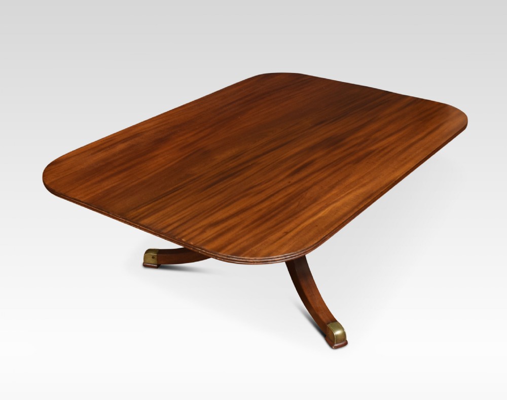 A low rectangular mahogany coffee table with rounded corners, resting on a central turned pedestal base with four splayed legs tipped with brass caps. View II