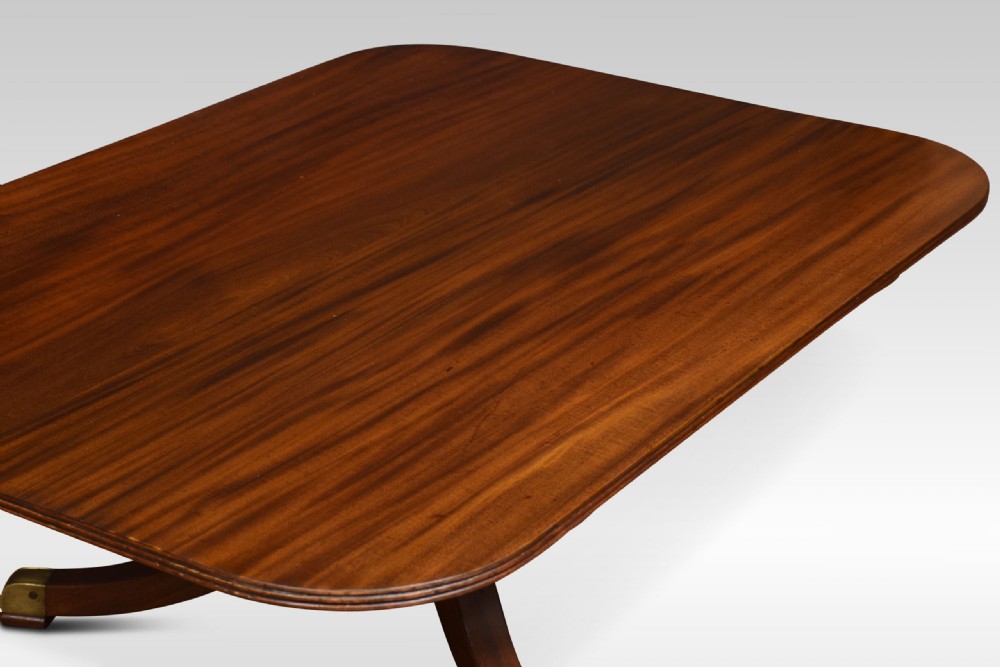 A low rectangular mahogany coffee table with rounded corners, resting on a central turned pedestal base with four splayed legs tipped with brass caps. View III