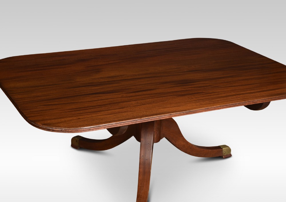 A low rectangular mahogany coffee table with rounded corners, resting on a central turned pedestal base with four splayed legs tipped with brass caps. View IV
