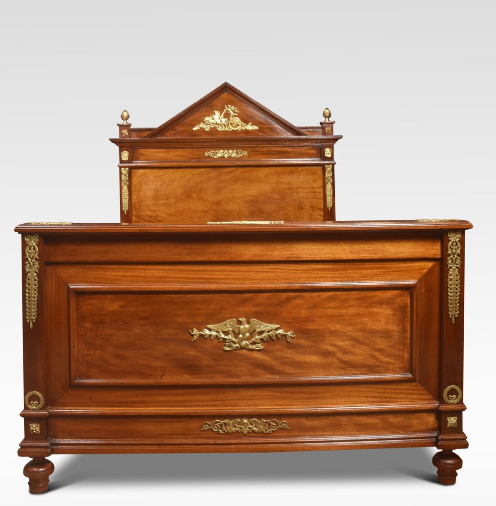 A French Empire style mahogany double bed frame featuring gilt brass mounts, turned feet, and a pediment headboard.