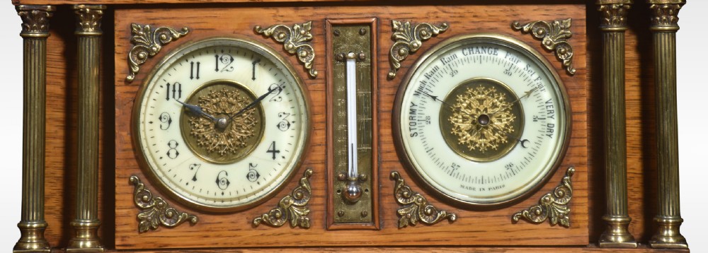 An architectural oak desk clock featuring a triangular pediment top, brass fluted columns, a central thermometer, and twin dials for a clock and barometer. View II