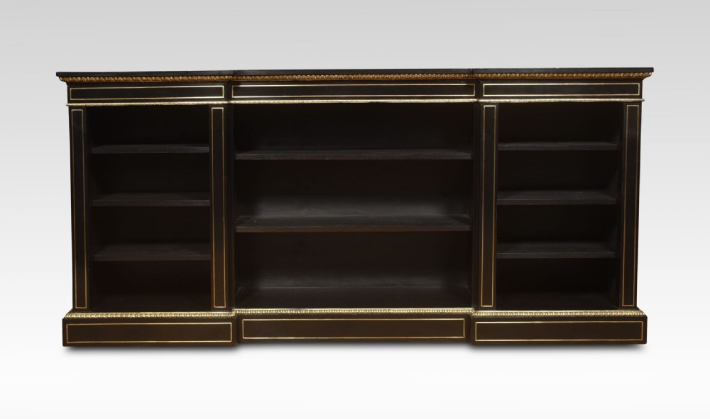 A large, low ebonised black wooden open bookcase featuring three sections outlined with decorative gilt brass mounts.