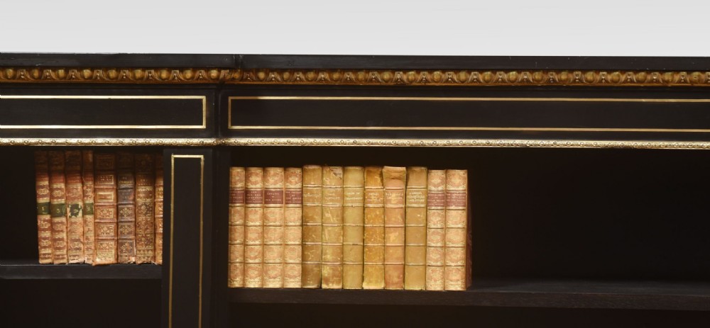 A large, low ebonised black wooden open bookcase featuring three sections outlined with decorative gilt brass mounts. View III