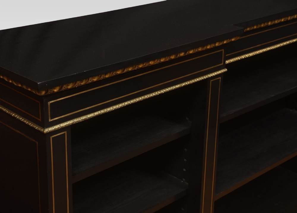 A large, low ebonised black wooden open bookcase featuring three sections outlined with decorative gilt brass mounts. View V