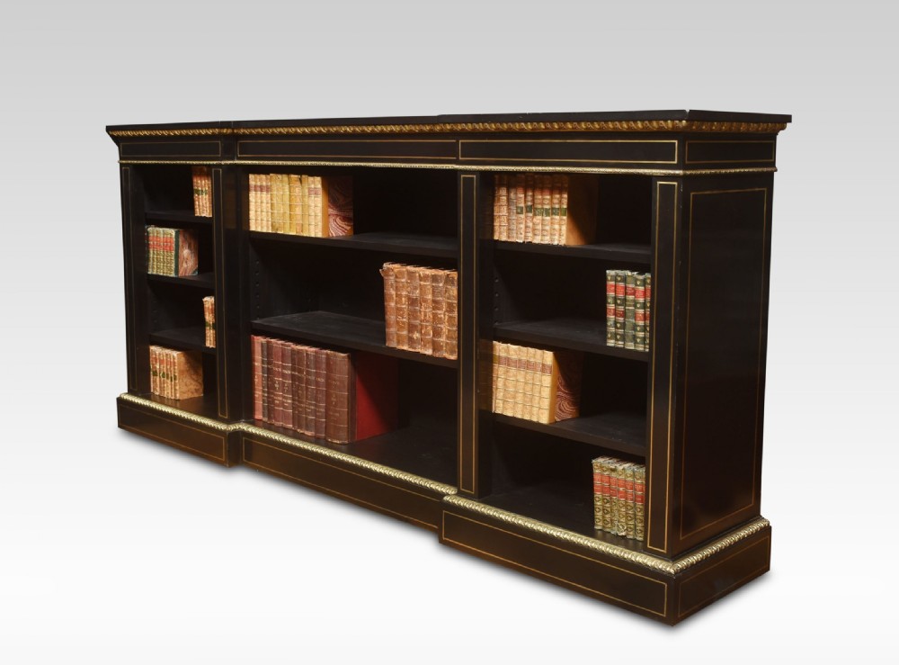 A large, low ebonised black wooden open bookcase featuring three sections outlined with decorative gilt brass mounts. View VI