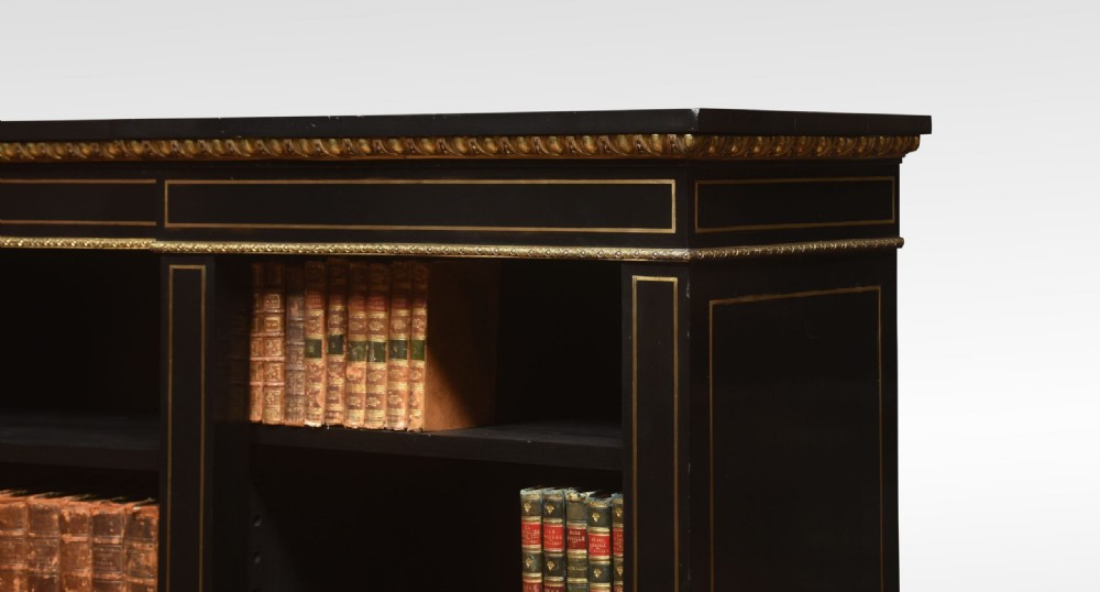 A large, low ebonised black wooden open bookcase featuring three sections outlined with decorative gilt brass mounts. View VII