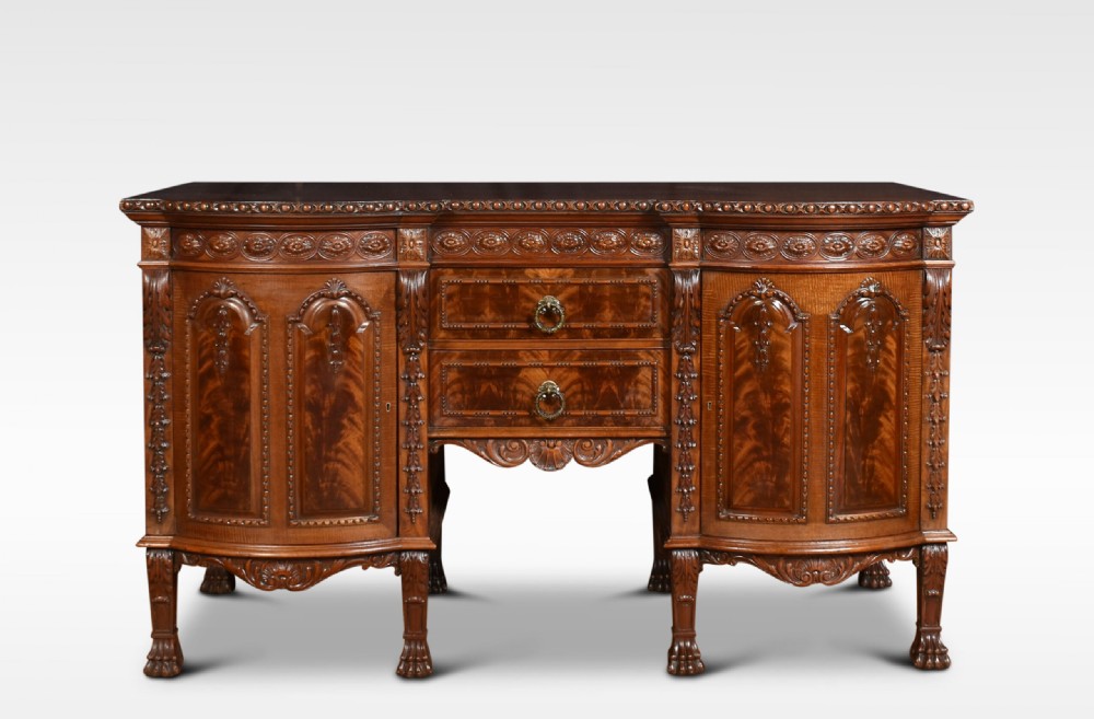 A deep brown mahogany inverted breakfront sideboard featuring carved accents, flame mahogany door panels, two central drawers, and carved claw-and-ball feet.