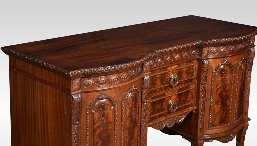 A deep brown mahogany inverted breakfront sideboard featuring carved accents, flame mahogany door panels, two central drawers, and carved claw-and-ball feet. View VII