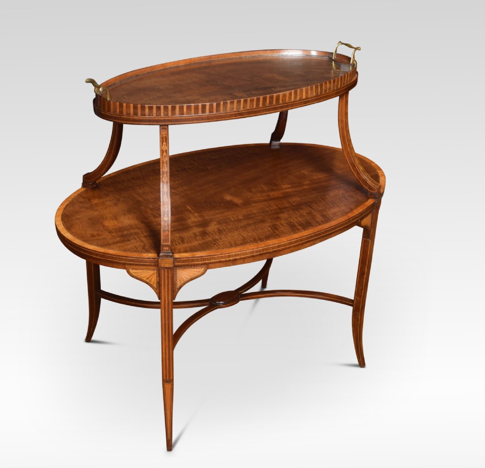 An oval two-tiered mahogany etagere table featuring satinwood crossbanded borders, fan inlays, sweeping upper supports, and twin brass handles on the top shelf.