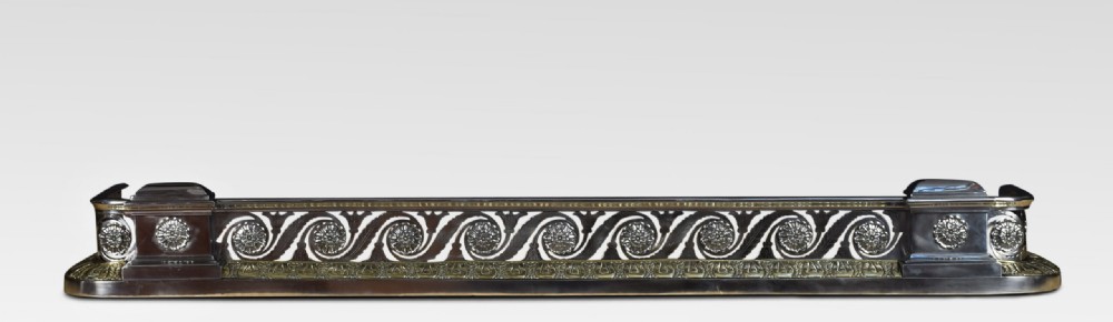 A Regency period fireplace fender constructed from polished steel and brass with Vitruvian scrollwork and rosette mounts. View II