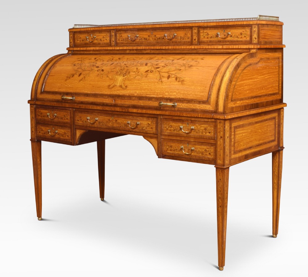 A Sheraton Revival satinwood cylinder bureau featuring detailed floral marquetry inlays, a curved roll-top front, brass gallery, and multiple drawers raised on tapered square legs.
