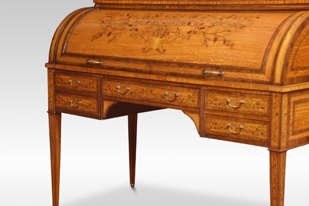 A Sheraton Revival satinwood cylinder bureau featuring detailed floral marquetry inlays, a curved roll-top front, brass gallery, and multiple drawers raised on tapered square legs. View II