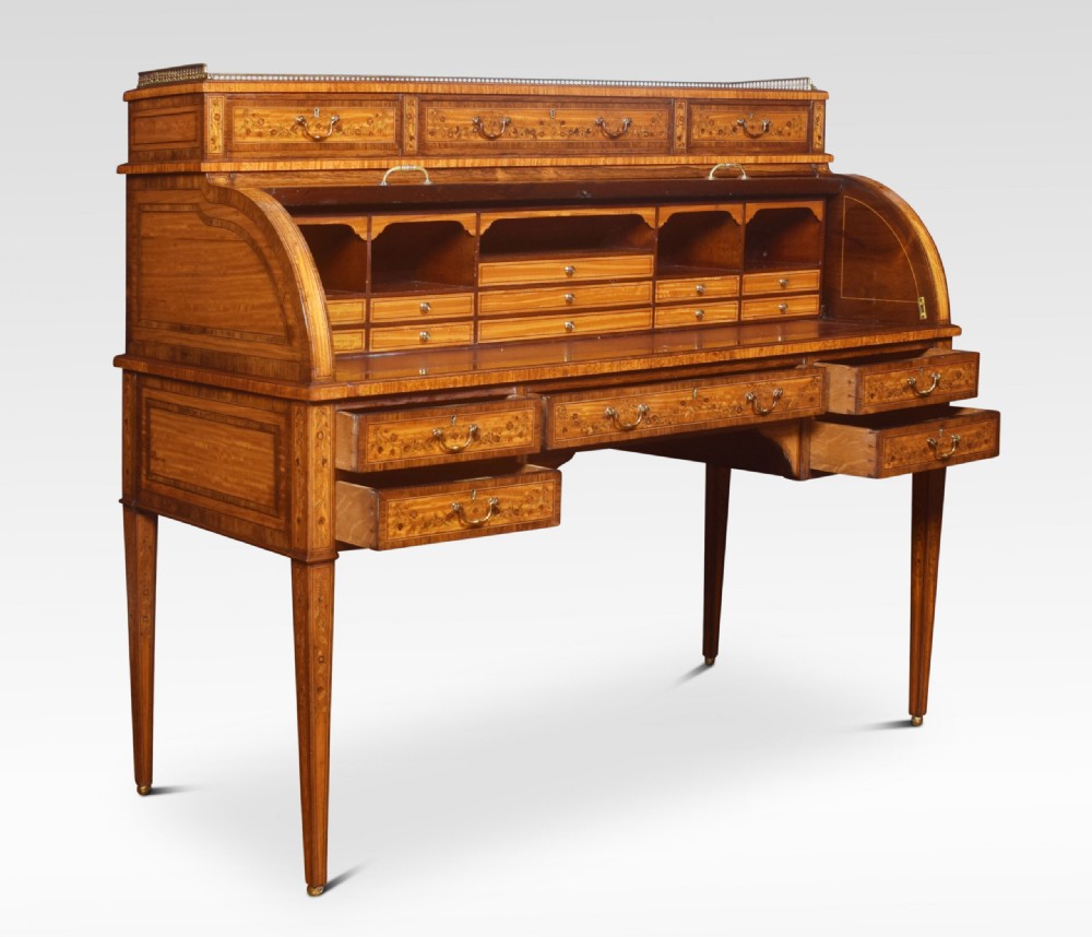 A Sheraton Revival satinwood cylinder bureau featuring detailed floral marquetry inlays, a curved roll-top front, brass gallery, and multiple drawers raised on tapered square legs. View VII